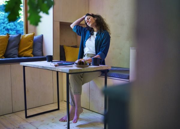 A woman with coffee sitting and stretching indoors in a tree house, weekend away concept.