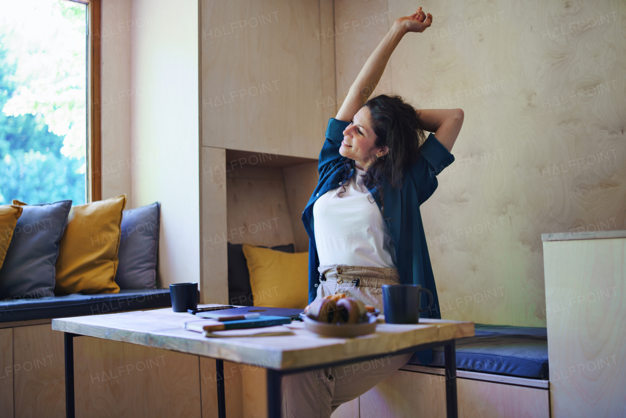 A Happy young woman with coffee sitting and stretching indoors in a tree house, weekend away and individual traveling concept.