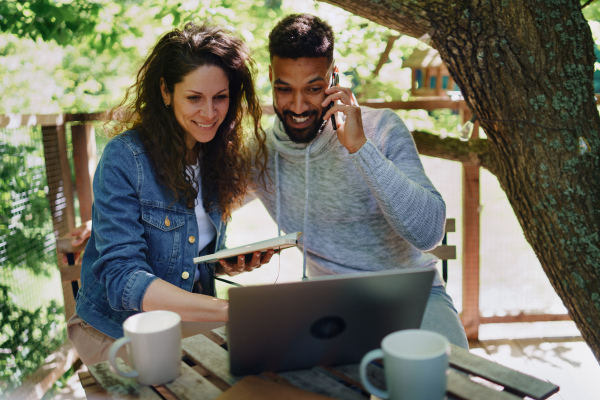 A happy couple with laptop resting outdoors in a tree house, weekend away and remote office concept.