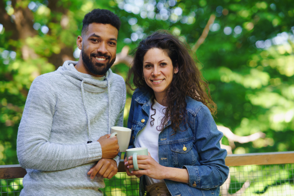 A happy couple resting and looking at camera outdoors in a tree house, weekend away and digital detox concept.