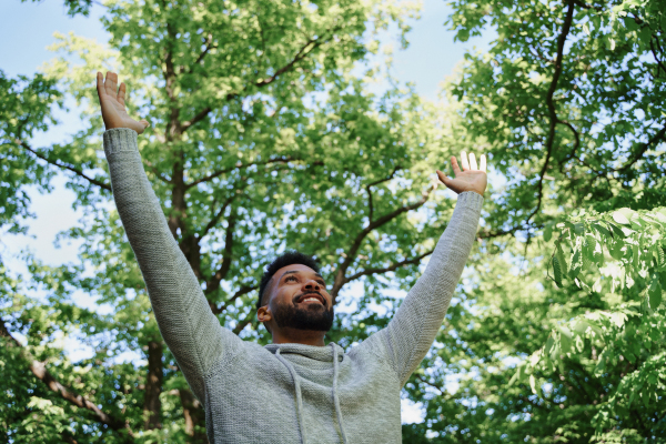 A low angle view of happy young man doing stretching exercise outdoors in forest, weekend away and digital detox concept.