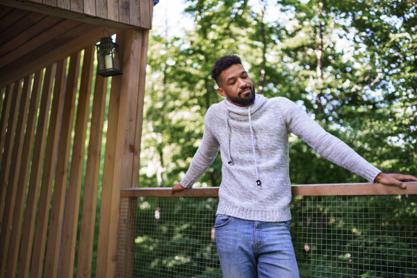 A happy young man resting outdoors outdoors on terrace of tree house, weekend away and digital detox concept.