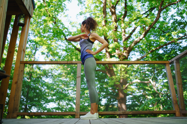 A happy mid adult woman doing exercise outdoors on terrace of tree house, weekend away and digital detox concept.