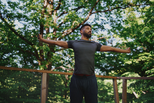 A low angle view of happy young man doing exercise outdoors on terrace of tree house, weekend away and digital detox concept.