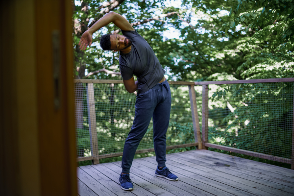 A young man doing exercise outdoors on terrace of tree house, weekend away and digital detox concept.