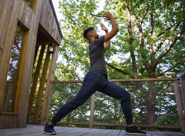 A young man doing exercise outdoors on terrace of tree house, weekend away and digital detox concept.