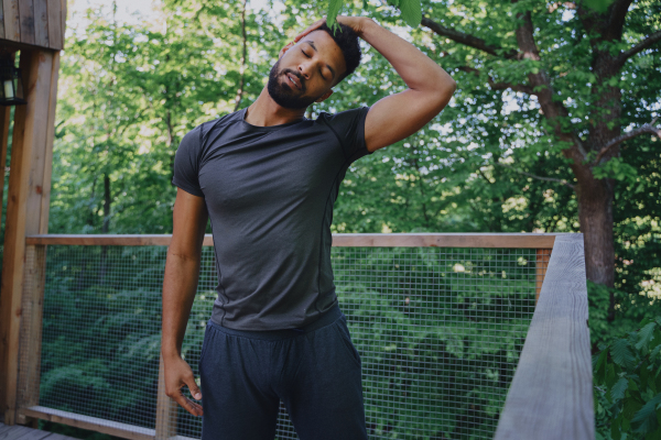 A young man doing exercise outdoors on terrace of tree house, weekend away and digital detox concept.