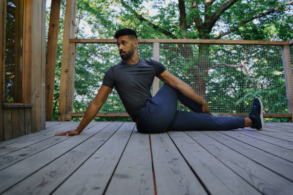 A happy young man doing exercise outdoors on terrace of tree house, weekend away and digital detox concept.