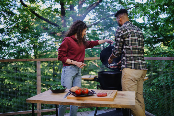 A happy biracial couple resting and preparing burgers outdoors in a tree house, weekend away and digital detox concept.