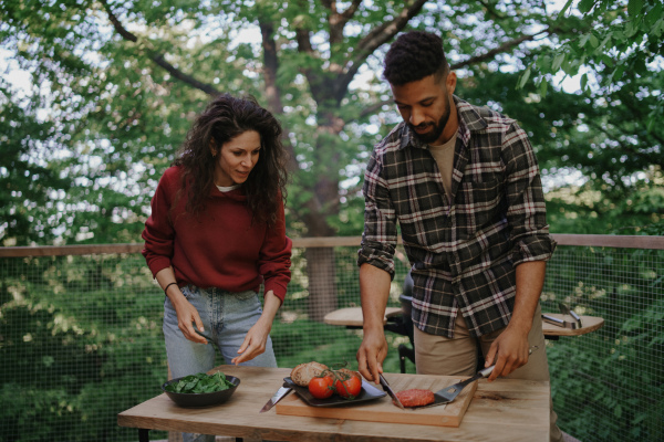 A happy biracial couple resting and preparing burgers outdoors in a tree house, weekend away and digital detox concept.