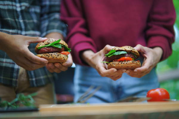 A close up of unrecognizable couple holding burgers outdoors in a tree house, weekend away and digital detox concept.