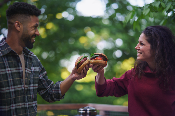 A happy couple resting and eating burgers outdoors in a tree house, weekend away and digital detox concept.