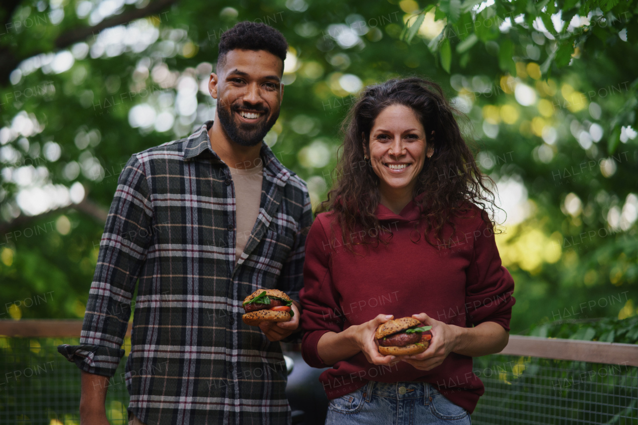 A happy couple resting and eating burgers outdoors in a tree house, weekend away and digital detox concept.