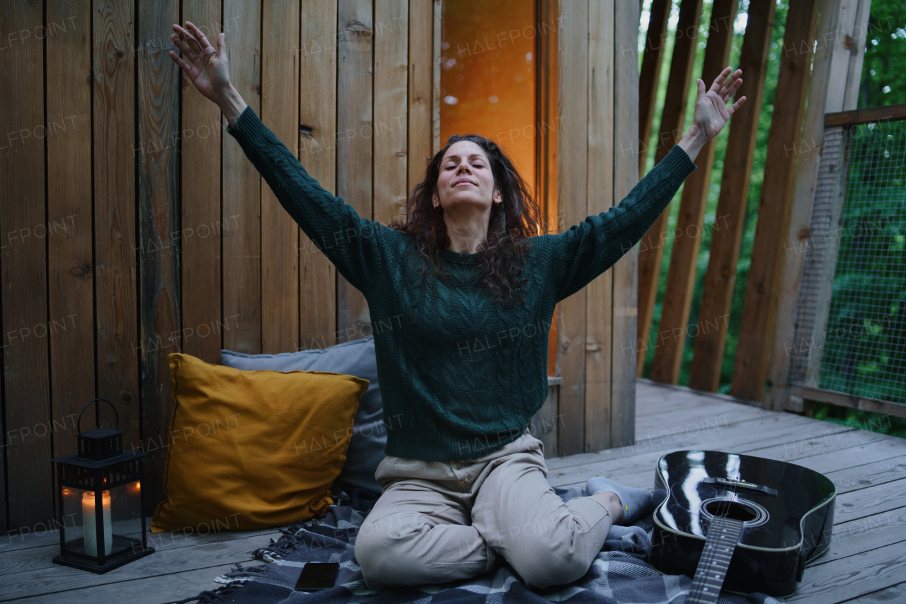 A happy mid adult woman resting and stretching outdoors in a tree house, weekend away and digital detox concept.