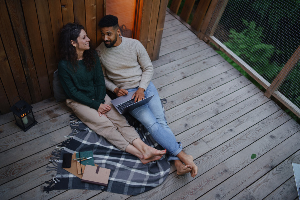 A top view of happy couple with laptop resting outdoors in a tree house, weekend away and remote office concept.