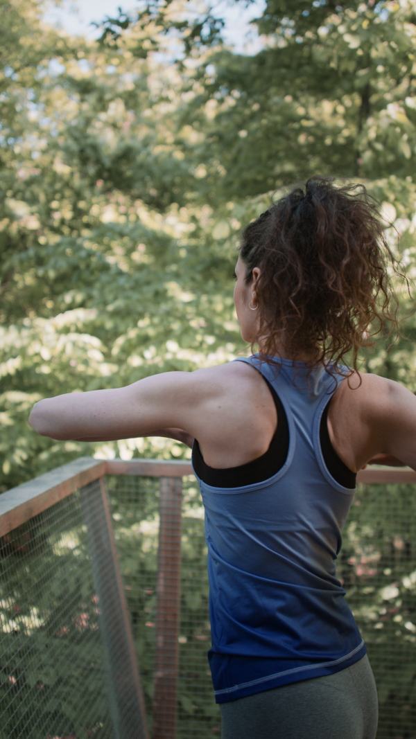 A vertical footage of happy mid adult woman doing exercise outdoors on terrace of tree house, weekend away and digital detox concept.