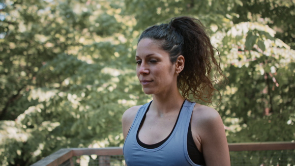 A happy mid adult woman doing exercise outdoors on terrace of tree house, looking at camera. Weekend away and digital detox concept.