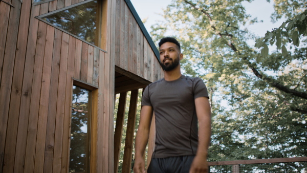 A happy young man doing exercise outdoors on terrace of tree house, weekend away and digital detox concept.