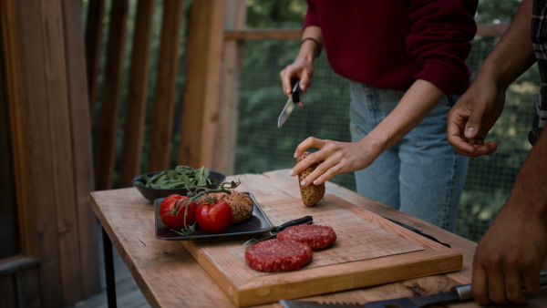 An unrecognizable couple resting and preparing burgers outdoors in a tree house, weekend away and digital detox concept.