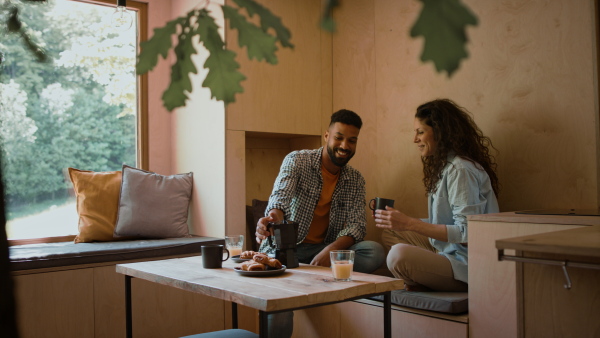 A happy couple in love sitting, resting and talking indoors in a tree house, weekend away and digital detox concept.