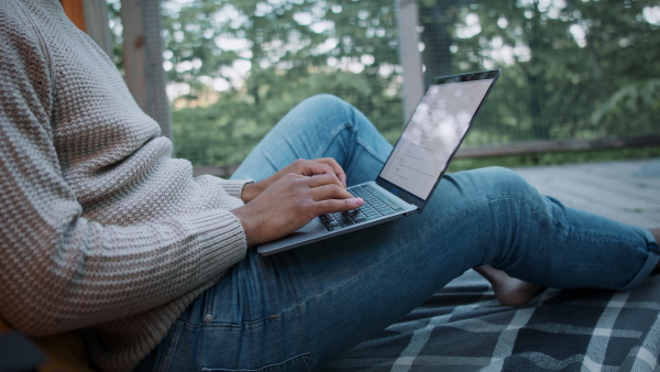 A close up of young man with laptop resting outdoors in a tree house, weekend away and remote office concept.