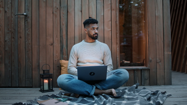 A happy young man with laptop resting outdoors in a tree house, weekend away and remote office concept.