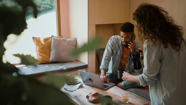 A happy couple in love having breakfast together indoors in a tree house, weekend away and digital detox concept.