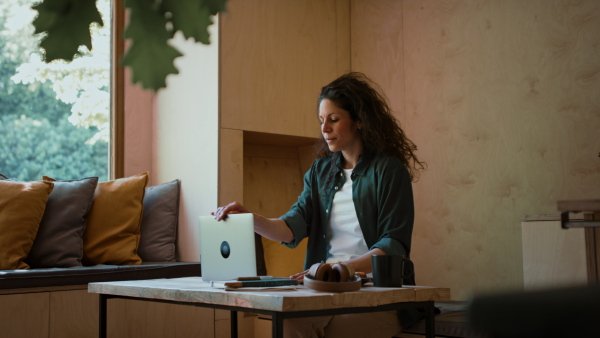 A happy young woman drinking coffee after finishing indoors in a tree house, weekend away and remote office concept.