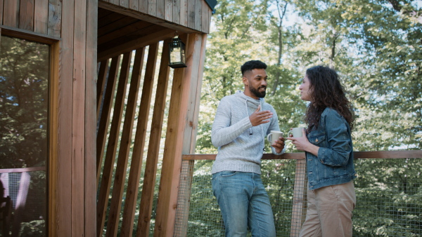 A happy couple resting and talking outdoors in a tree house, weekend away and digital detox concept.