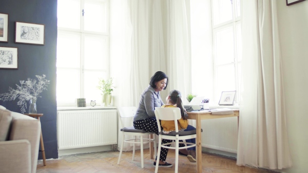 A happy small girl with grandmother sitting at table at home, using typewriter.