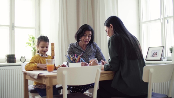 A small girl with mother and grandmother sitting at the table at home, playing games.