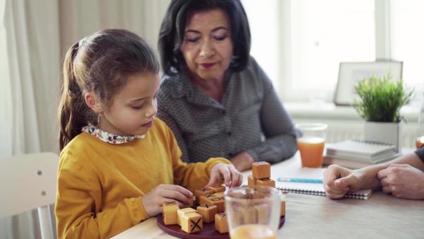 A small girl with mother and grandmother sitting at the table at home, playing games.