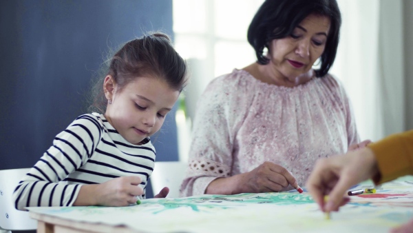 A small girl with mother and grandmother sitting at the table at home, painting pictures.