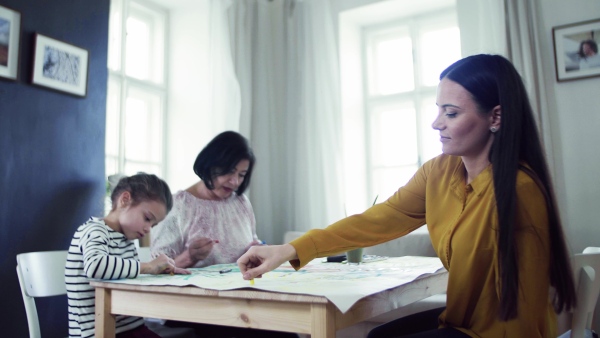 A small girl with mother and grandmother sitting at the table at home, painting pictures.