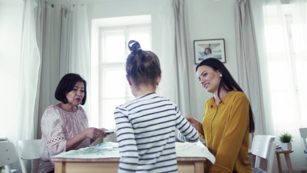 A small girl with mother and grandmother sitting at the table at home, painting pictures.