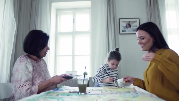 A small girl with mother and grandmother sitting at the table at home, painting pictures.