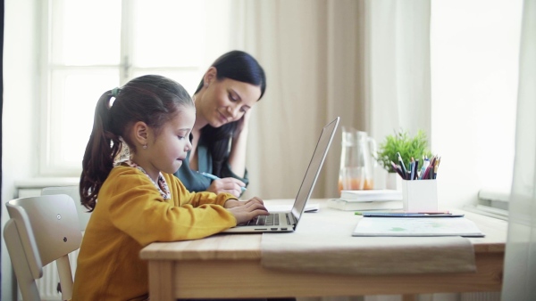 A happy small girl with mother sitting at table at home, using laptop. Slow motion.