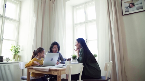 A happy small girl with mother and mother sitting at table at home, using laptop. Slow motion.