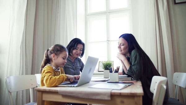 A happy small girl with mother and mother sitting at table at home, using laptop. Slow motion.