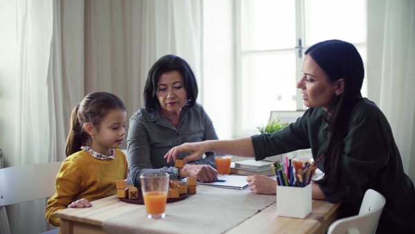 A small girl with mother and grandmother sitting at the table at home, playing games. Slow motion.