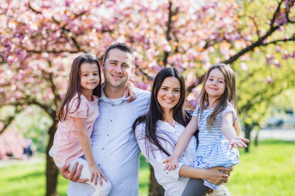 Front view of young parents with small daugthers standing outside in spring nature.