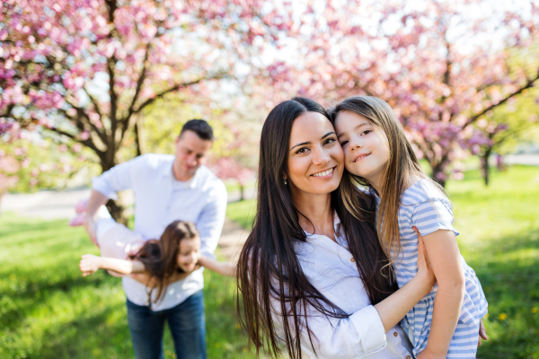 Family of young parents with small daugthers standing outside in spring nature, having fun.