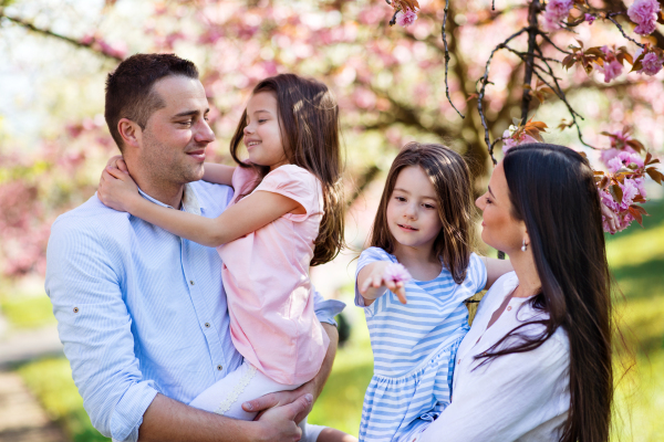 Front view of young parents with small daugthers standing outside in spring nature.