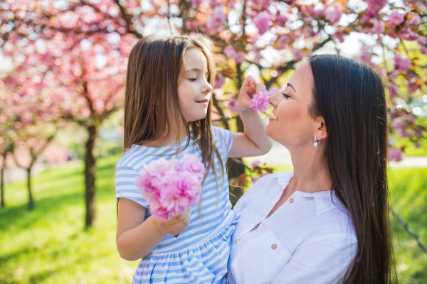 A young mother holding small daughter outside in spring nature.