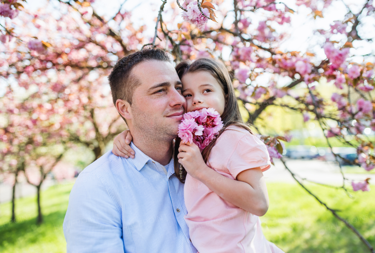 A young father holding small daughter outside in spring nature.