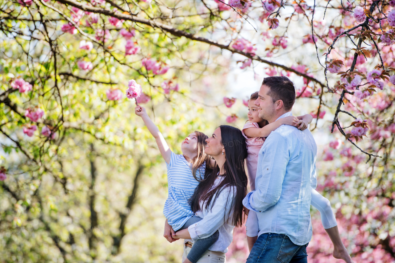 Side view of young parents with small daugthers standing outside in spring nature.