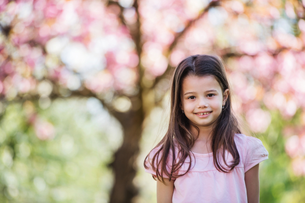 A cheerful small girl standing outside in spring nature, looking at camera.