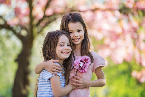 Two small girls standing outside in spring nature, hugging. Copy space.