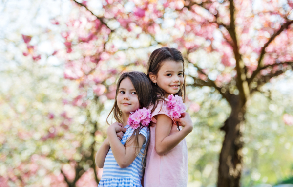 Two small girls with flowers standing outside in spring nature, looking at camera.