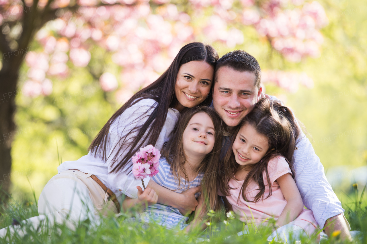 Front view of young parents with small daugthers sitting outside in spring nature.